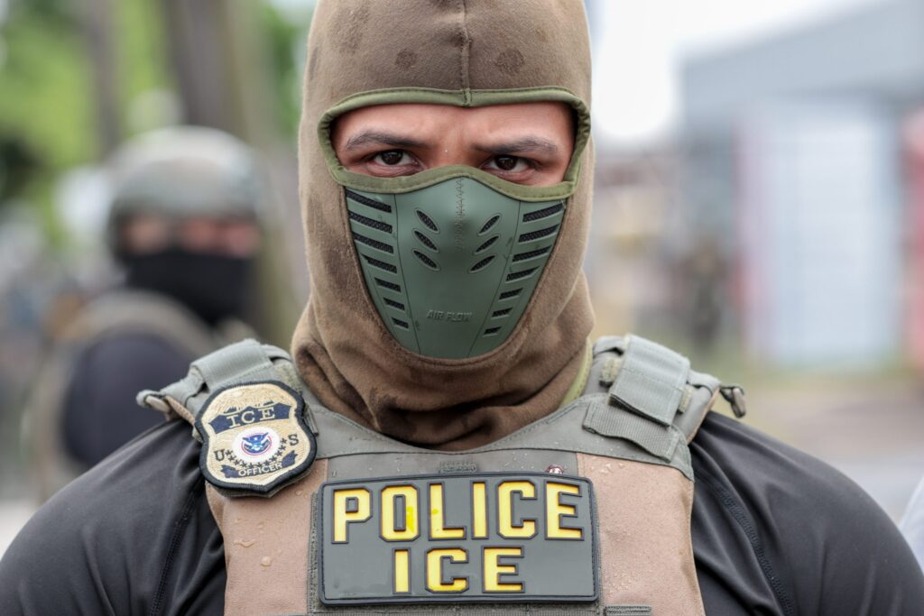 On June 10, 2026, President Donald Trump signed into law a bill providing $70 billion for immigration enforcement and detention activites over the next three years. In this photo, a U.S. Immigration and Customs Enforcement agent watches a crowd of protesters at Delaney Hall in Newark, N.J., on May 25, 2026. (Photo by Ben Ackman/New Jersey Monitor)