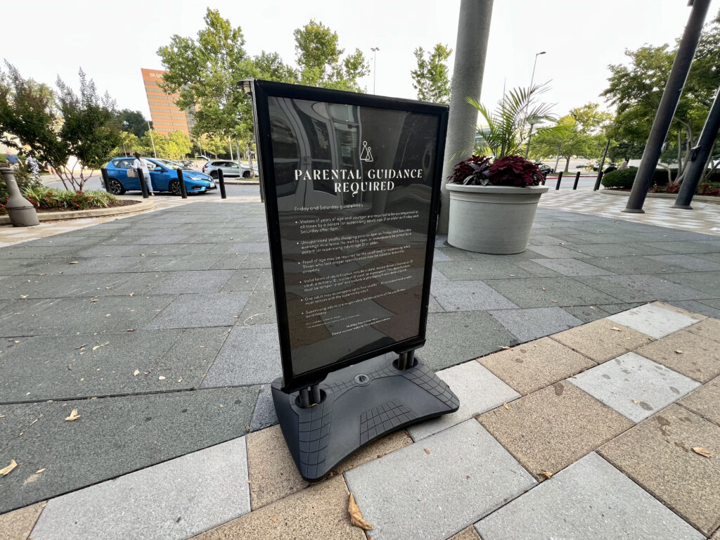 A sign at the Mall in Columbia, a suburban shopping center in central Maryland, requires anyone under 17 to be accompanied by a parent or supervising adult on Friday and Saturday evenings. Public spaces and commercial areas across the country are increasingly imposing curfews and other restrictions on young people. (Photo by Amanda Watford/Stateline)